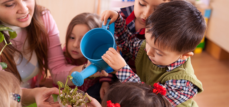 Child using a watering can to water a plant