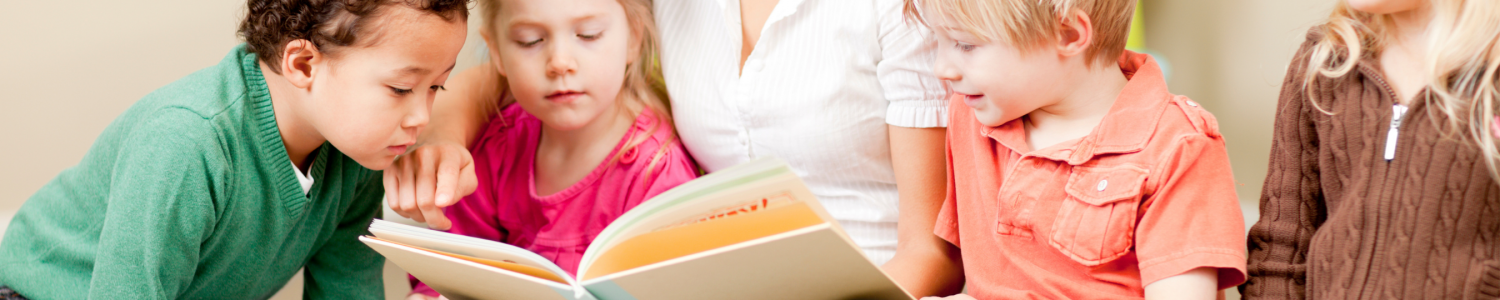 Image of educator seated with four young children reading a story.