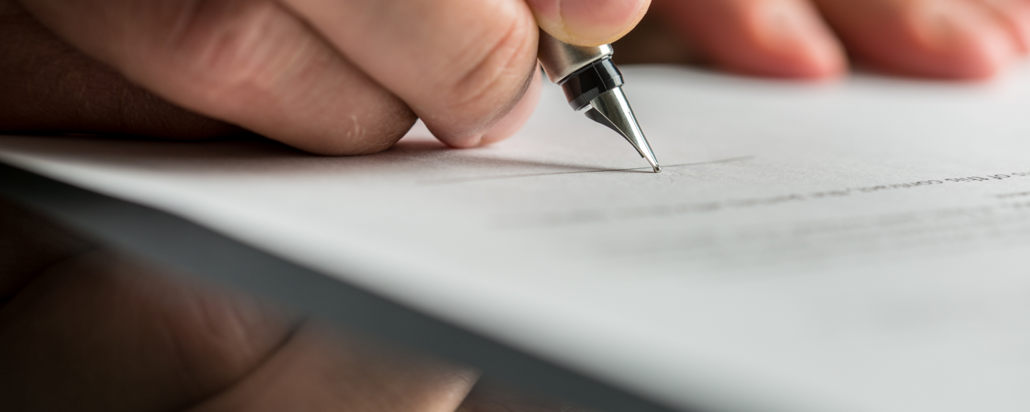 Image of person's hand signing a document with a pen.