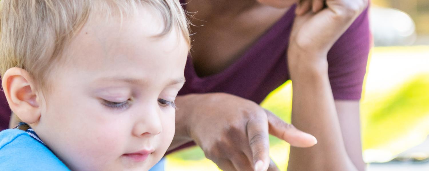 Educator sitting with a child overlooking as they play