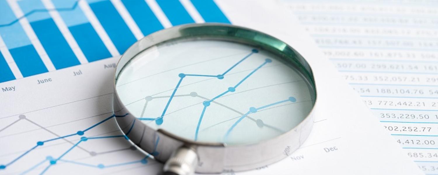 A series of line and bar graphs on paper with a magnifying glass sitting on top