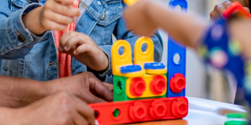 Children sitting around a table playing with building blocks. The image is closely cropped so you can only see their hands.