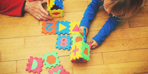 Child and adult playing with a large floor puzzle on hardwood floor