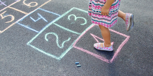 A young child is standing on one foot, on a hopscotch outline drawn on the ground