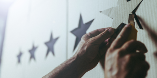 4 cardboard stars hung on wall. A pair of hands looks to be placing a fifth star. 