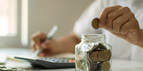 Person counting coins, writing with a pen and using a calculator.