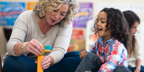 educator and child sitting on floor playing with blocks