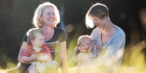 Two mothers sitting in a field, each holding a small child.