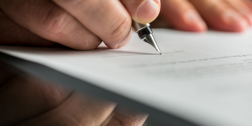 Image of person's hand signing a document with a pen.