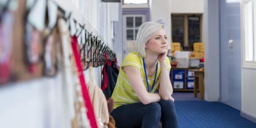 Stressed educator seated outside a classroom staring off into the distance