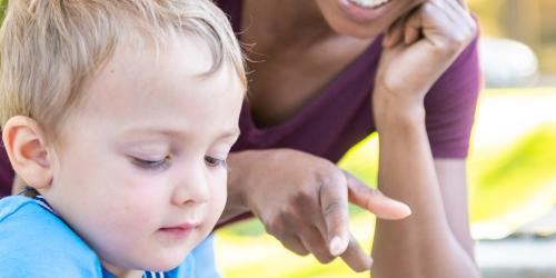 Educator sitting next to a child in an outdoor setting
