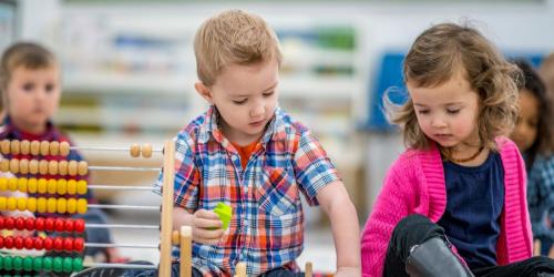 Young children playing together with stacking blocks and sliding beads