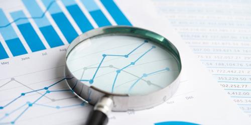 A series of line and bar graphs on paper with a magnifying glass sitting on top