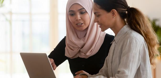 Muslim female mentoring her female colleague, pointing towards an open laptop