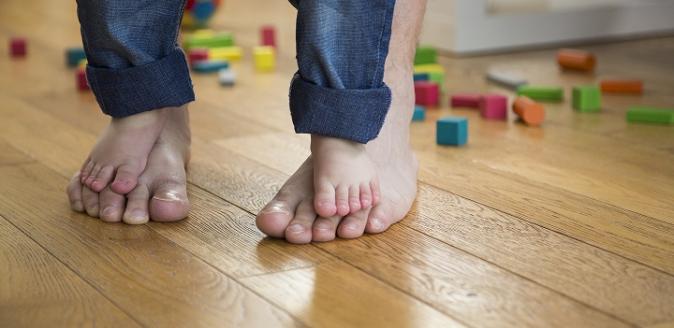 A child's bare feet standing on the top of an adult's bare feet