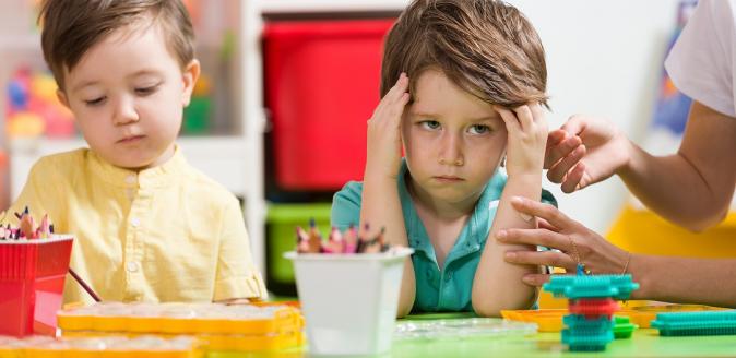 Angry, overwhelmed child sitting at a table, massaging his temples