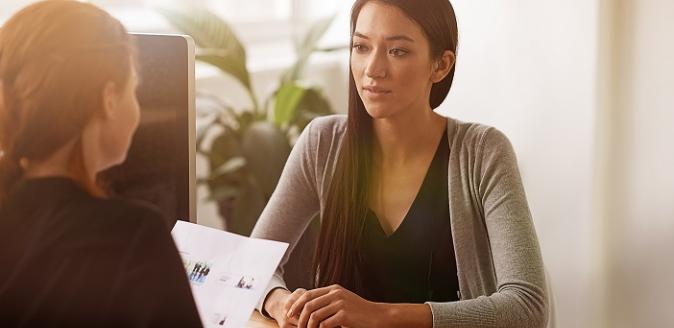 Woman sitting at a desk holding papers, interviewing another woman