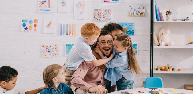 Children hugging happy educator at a table in a classroom setting