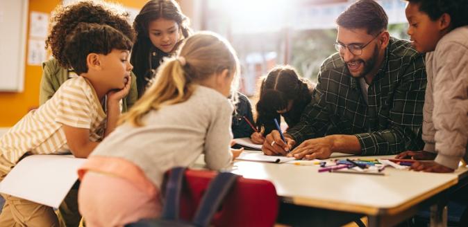 An educator and school-aged children using coloured pencils together at a table.