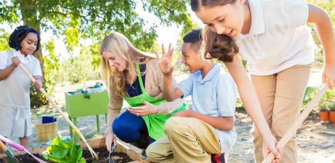 Educator and school aged children planting and digging in a garden bed