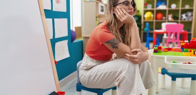 Educator sitting on a child's chair, resting their chin in one hand and looking off in the distance