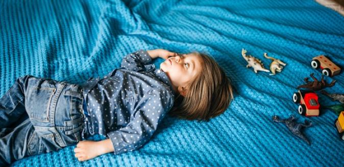 A child lying down on a blanket with eyes open, looking away from the camera
