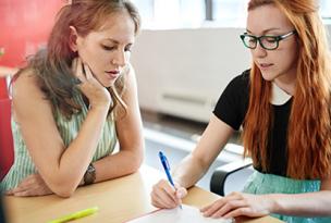 Two educators documenting ideas using a notepad and pens at a table