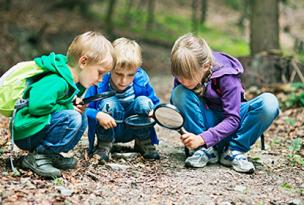 Three children with magnifying glasses crouched down and studying the ground