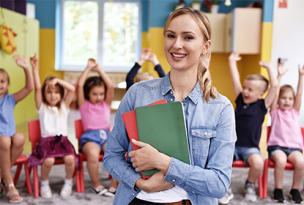 An educator holding books with children with cheerful hands in the air in the background of a classroom