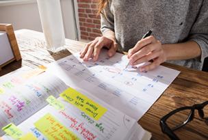 Educator's hands writing in appointments in a diary with open workbooks on the table