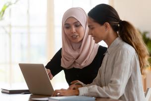 Muslim female mentoring her female colleague, pointing towards an open laptop