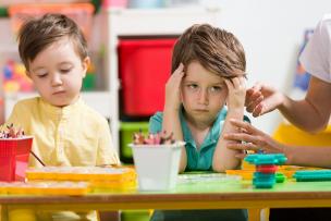 Angry, overwhelmed child sitting at a table, massaging his temples