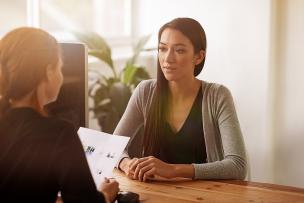 Woman sitting at a desk holding papers, interviewing another woman