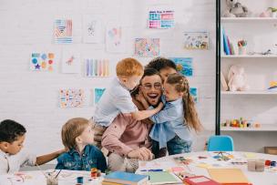Children hugging happy educator at a table in a classroom setting