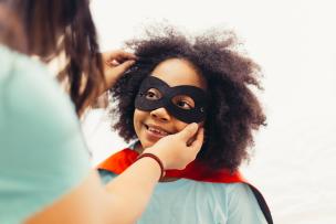 Educator helping a child put on a super hero mask