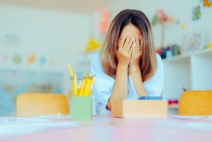 Distressed educator holding their face in their hands and covering their eyes